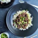 A black bowl containing Korean beef over sautéed cabbage and white rice.