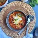 A bowl of pumpkin chili with sour cream, shredded cheddar, and jalapeños.