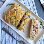 A white serving plate with a salmon Wellington, cut into serving slices.