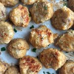 A parchment-lined tray containing baked chicken meatballs brushed in an herb butter.
