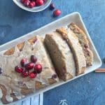 A Cranberry Eggnog Loaf on a white serving plate with slices cut out of it.