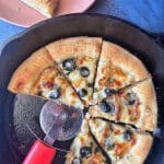 A cast iron skillet containing a pizza with two slices cut out of it.