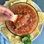 A hand dipping a corn tortilla into a bowl of 5-minute homemade chunky salsa.