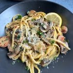 A plate of sausage and mushroom pasta with parmesan and a lemon slice.