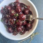 A fork piercing a stovetop party meatball over a bowl of a large serving of them.