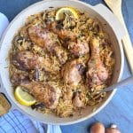 A cream colored skillet filled with baked chicken legs and mushroom-orzo pasta.