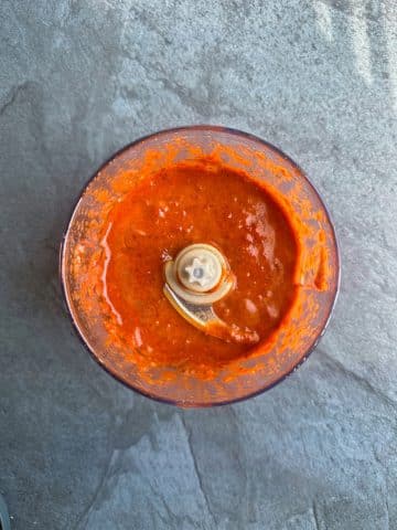 A food processor containing a blended red sauce.