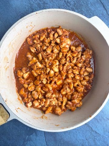 A skillet filled with cooked chopped chicken in a red sauce.