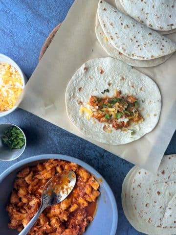 An assembly line of chicken tacos with the filling ingredients organized in bowls on the side.