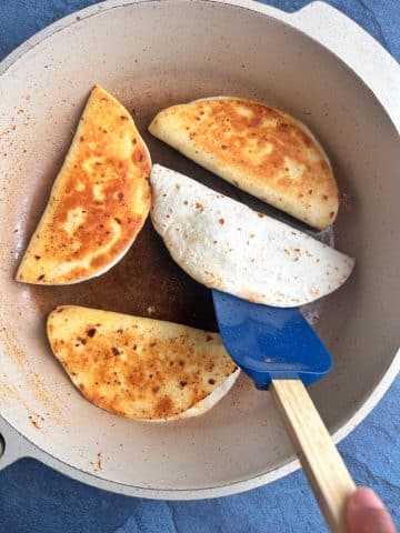 A skillet with 4 tacos being pan fried, and one being flipped with a spatula.