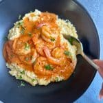 A black bowl filled with Cajun Shrimp and Grits, with a spoon scooping into the right side.