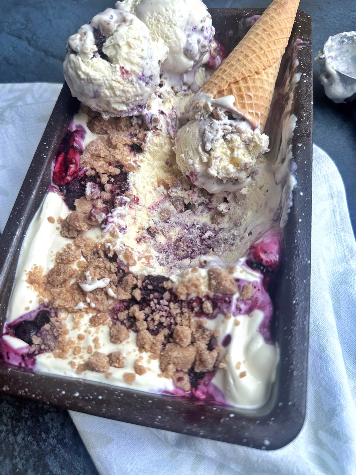 A loaf pan filled with Blueberry Crumble Ice cream, with a cone placed inside.