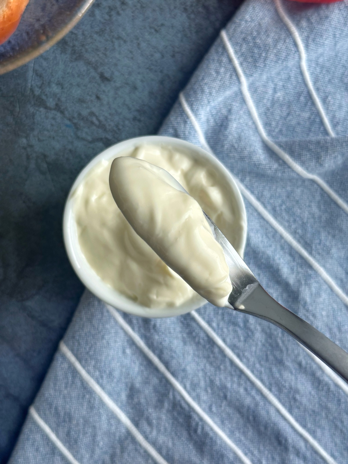 A knife displaying the texture of homemade mayo over a bowl of the spread.