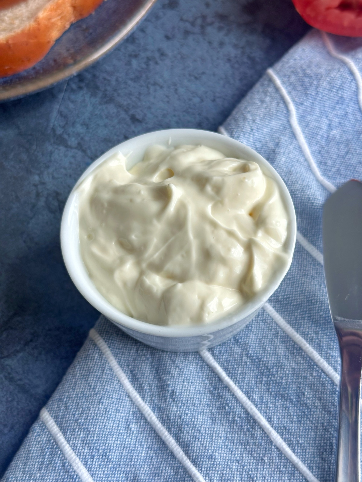 A bowl of mayonnaise sitting on a blue napkin.