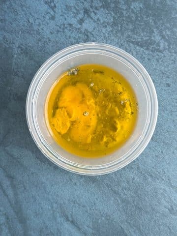 A deli container filled with one egg, oil, spices, and mustard.