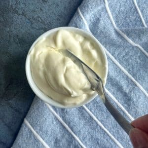 A small saucer filled with homemade mayonnaise and a butter knife being spread in the middle.