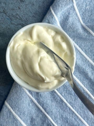A small saucer filled with homemade mayonnaise and a butter knife being spread in the middle.