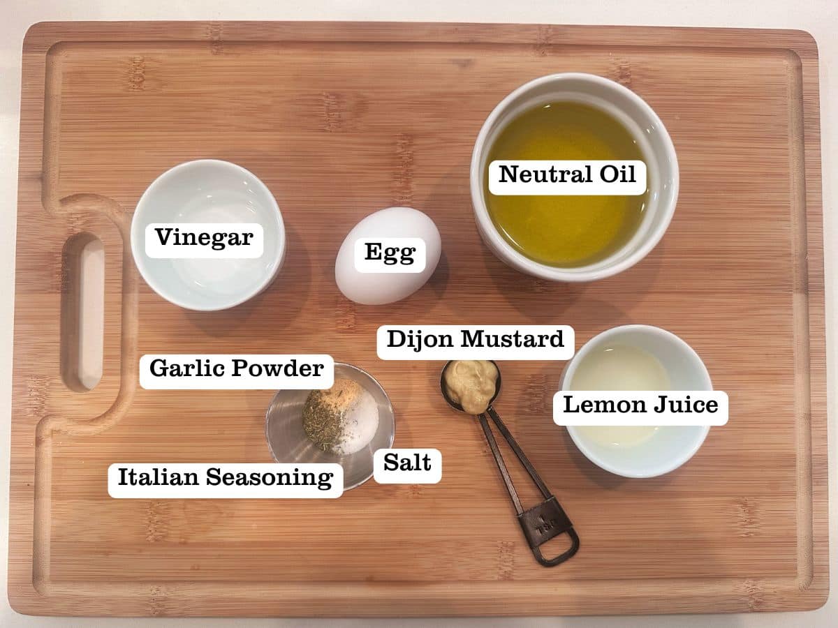 A wooden board containing ingredients including an egg, oil, dijon mustard, and white vinegar.