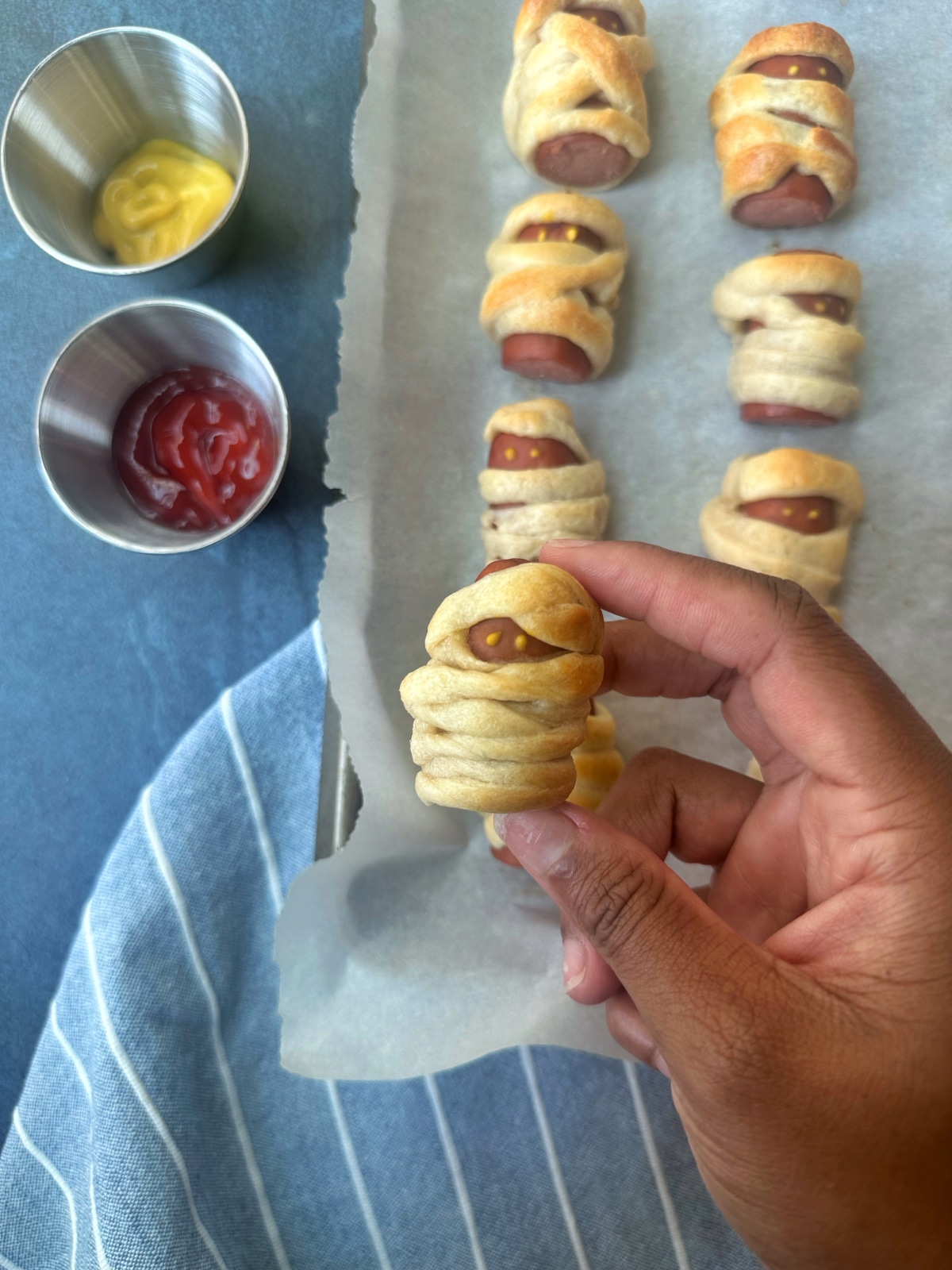 A hand holding a mini mummy dog with more on the pan in the background.