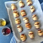 A pan containing mini pigs in a blanket, decorated like mummies with mustard "eyes".