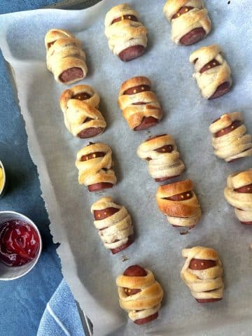 A pan containing mini pigs in a blanket, decorated like mummies with mustard "eyes".