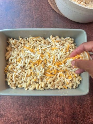 A hand sprinkling cheese into a pan of unbaked macaroni.