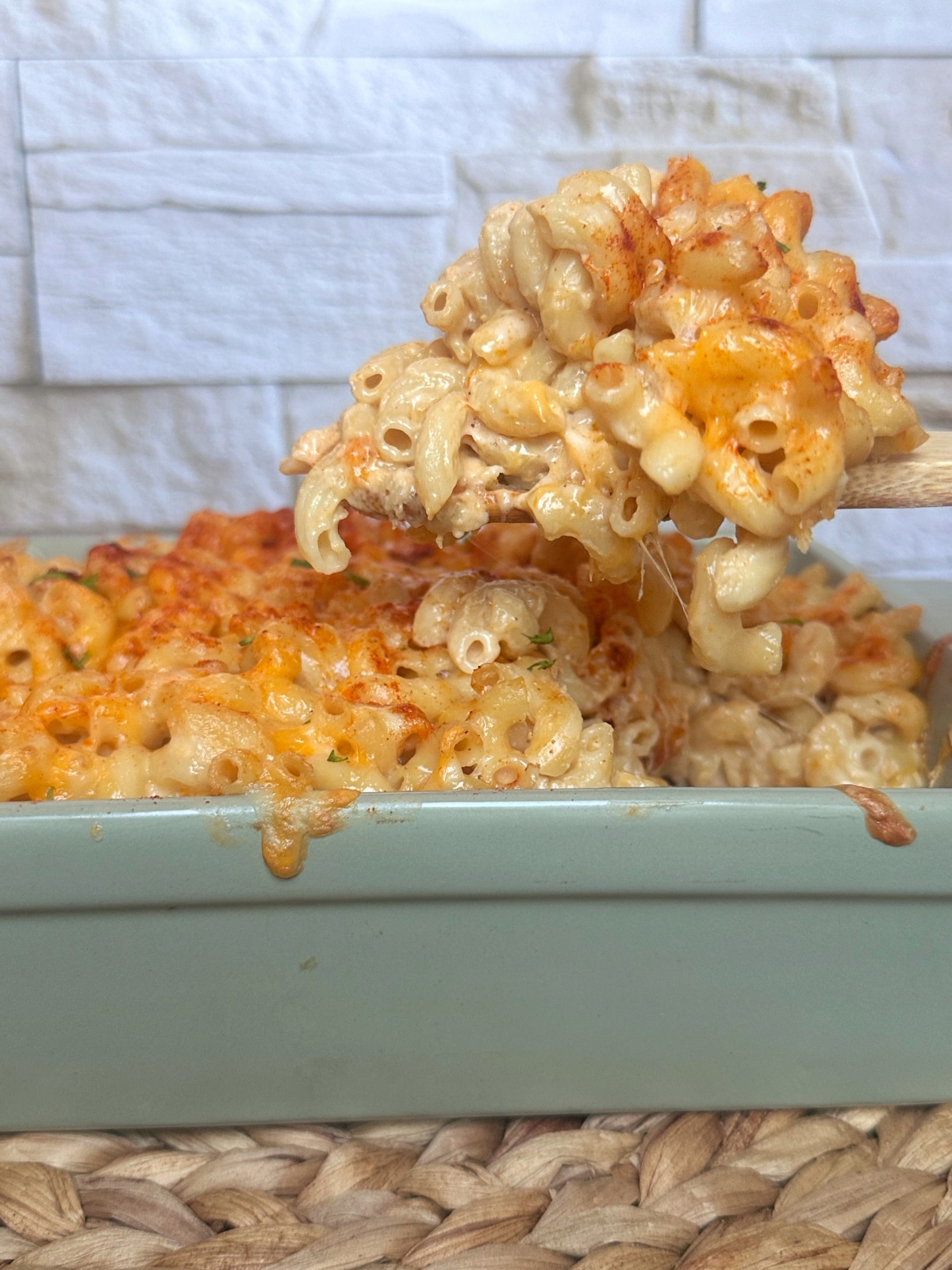 A wooden spoon holding a scoop of macaroni and cheese over a ceramic dish.