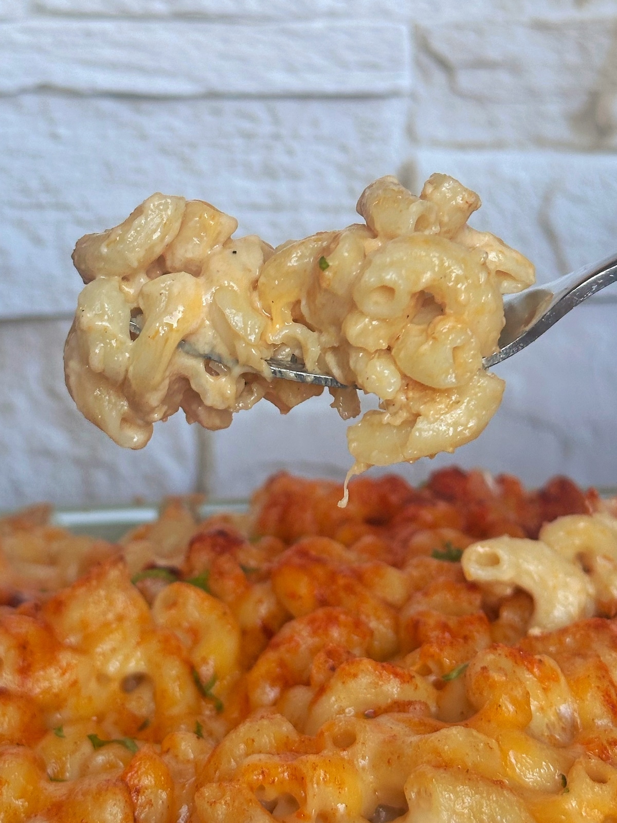 A fork displaying a portion of baked Mac and cheese over the pan.