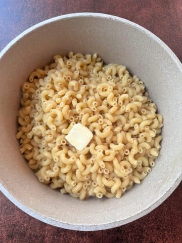 A pot of drained, cooked macaroni noodles with a knob of butter in the middle.