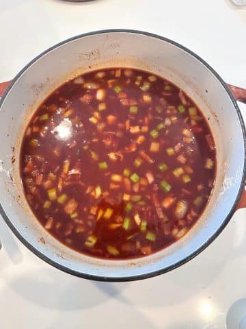 A dutch oven filled with a dark brown broth with mirepoix.