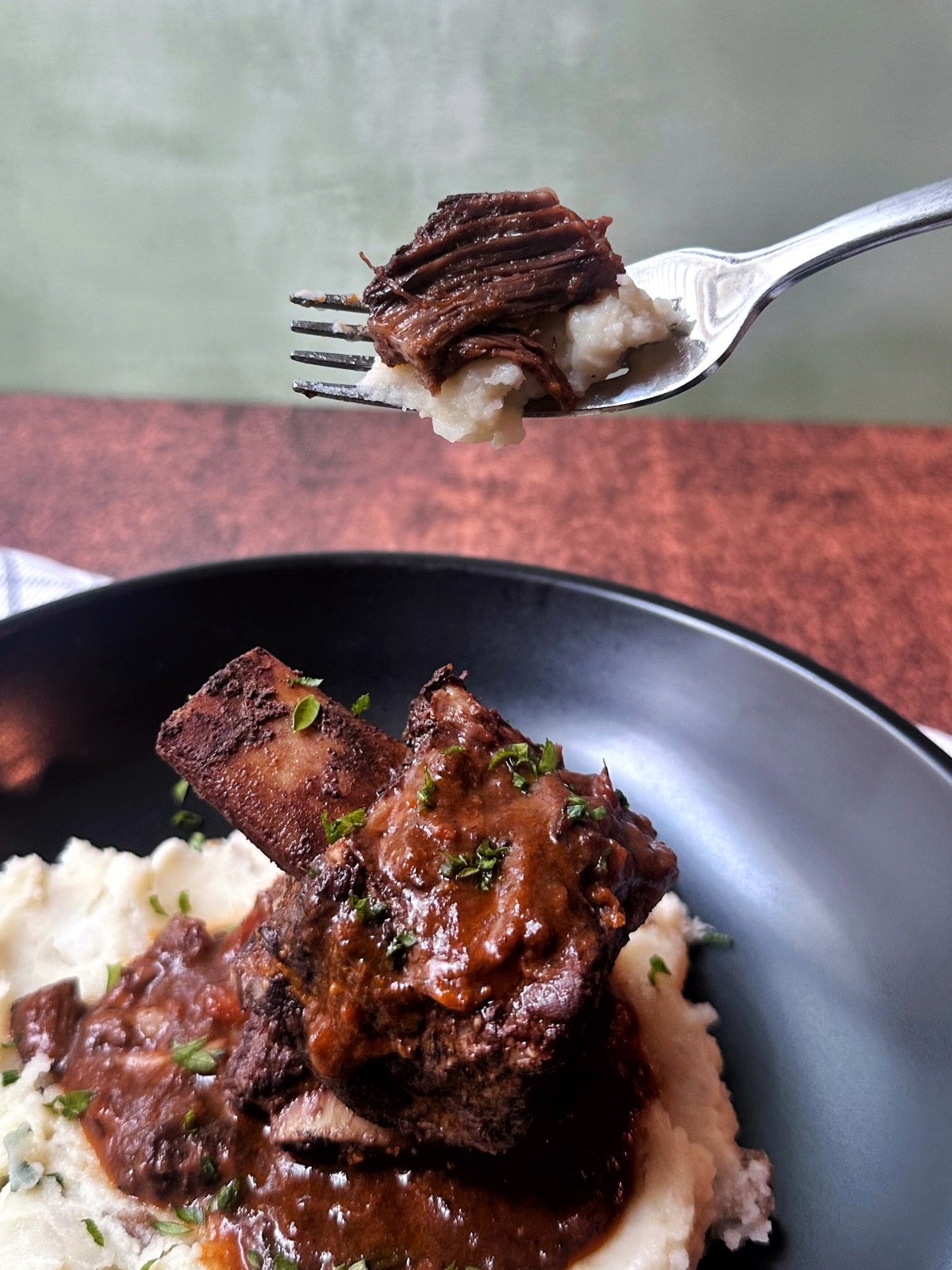 A fork holding up a piece of red wine braised short rib.