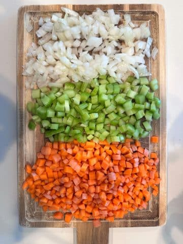 A wooden board containing diced mirepoix.