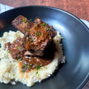 A black plate with mashed potatoes and two braised short ribs stacked on top.