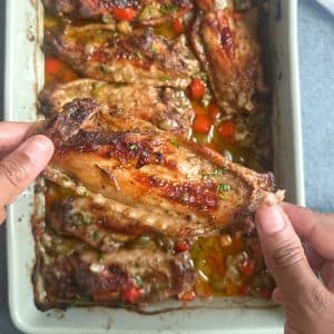 A pair of hands holding a Cajun Baked Turkey Wing up for display over the remaining wings in a pan.