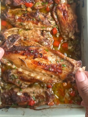 A pair of hands holding a Cajun Baked Turkey Wing up for display over the remaining wings in a pan.