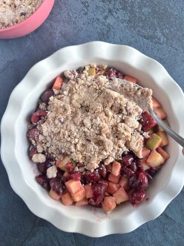 A fork spooning crisp topping onto a pie plate containing fruit filling.