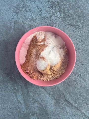 A mixing bowl containiner brown and white sugar, oats, pecans, and flour.