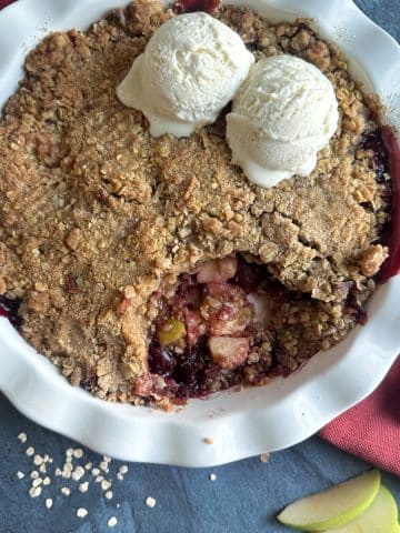 A pie pan filled with cherry apple crisp, and two scoops of ice cream on top.
