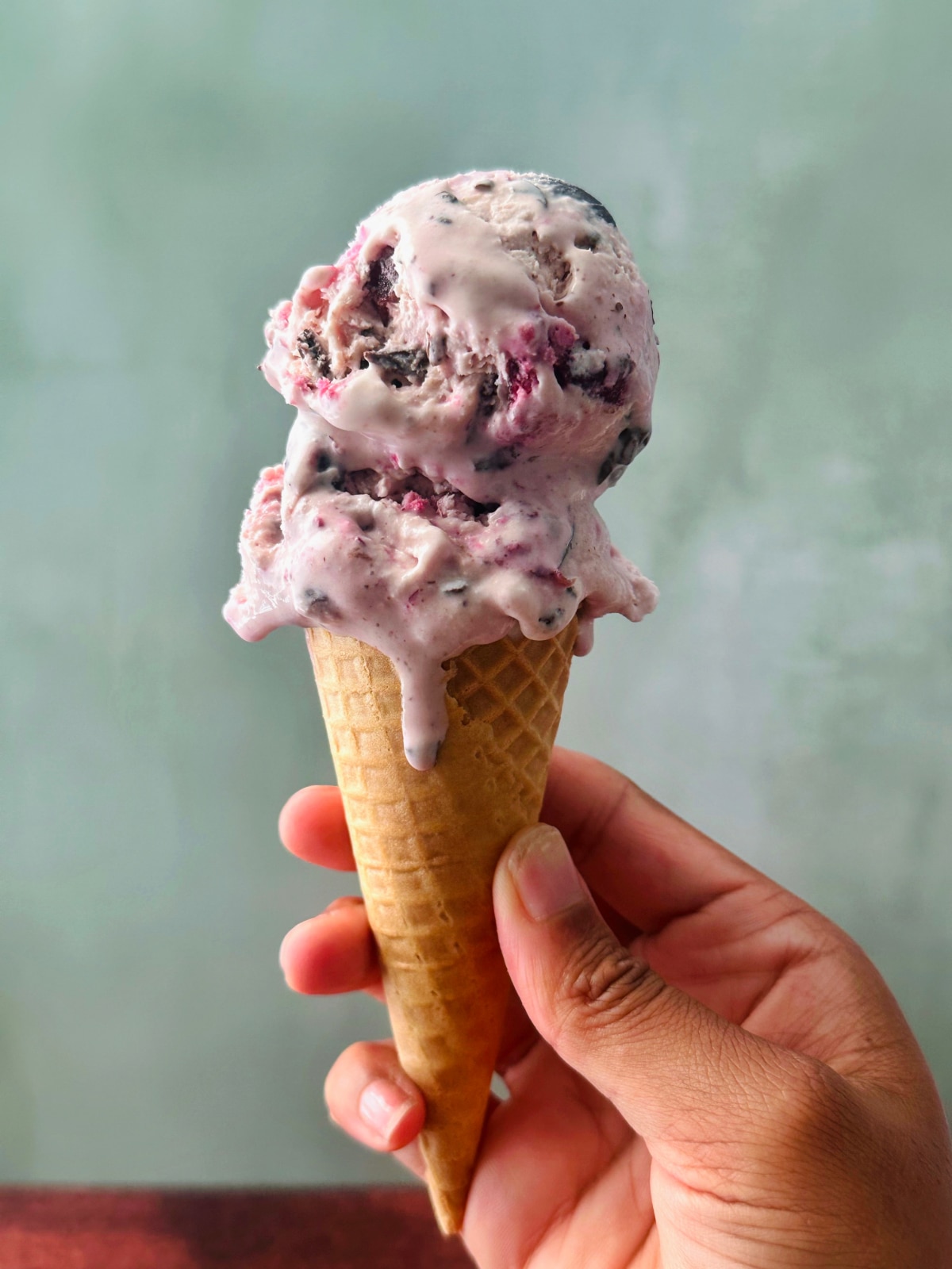 A hand holding up a cone filled with two scoops of cherry chip ice cream.