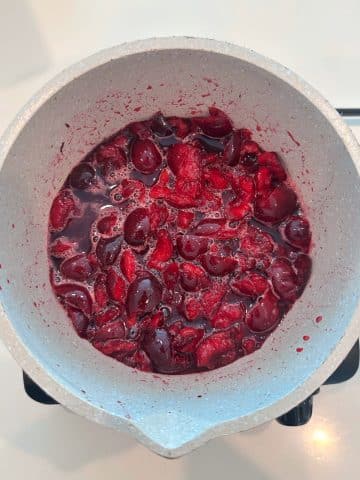 A pot containing cooked sweet dark cherries.