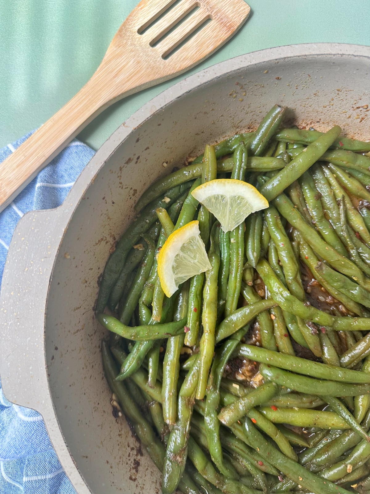 A cream colored pan filled with sautéed green beans and slices of lemon.