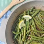 A pan containing cooked green beans with two lemon slices on top.
