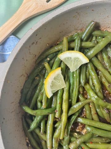 A pan containing cooked green beans with two lemon slices on top.