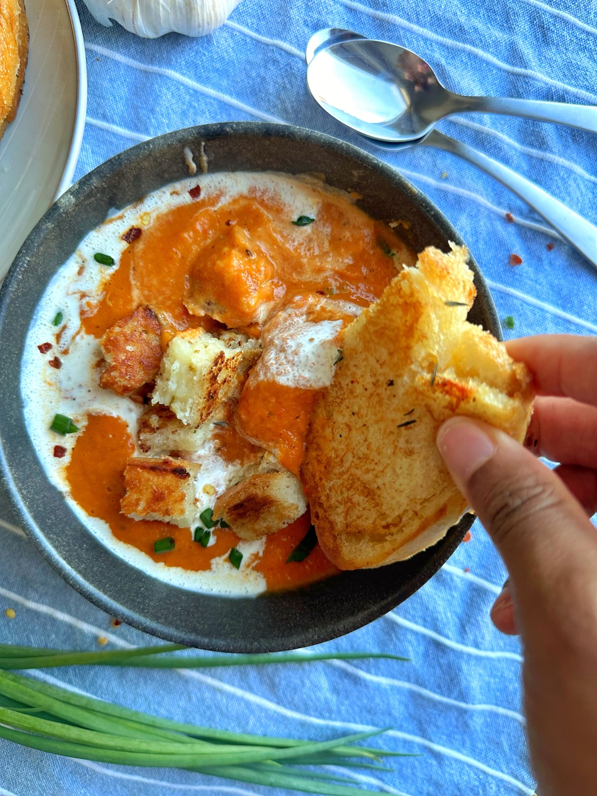 A hand dipping a piece of grilled cheese into a bowl of soup.