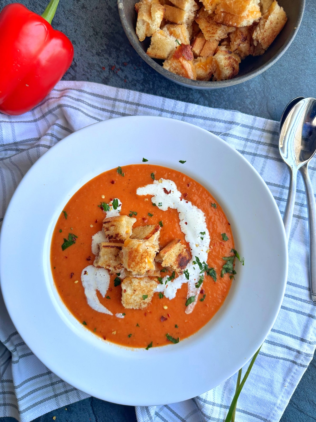 A bowl filled with roasted red pepper soup and croutons on top.