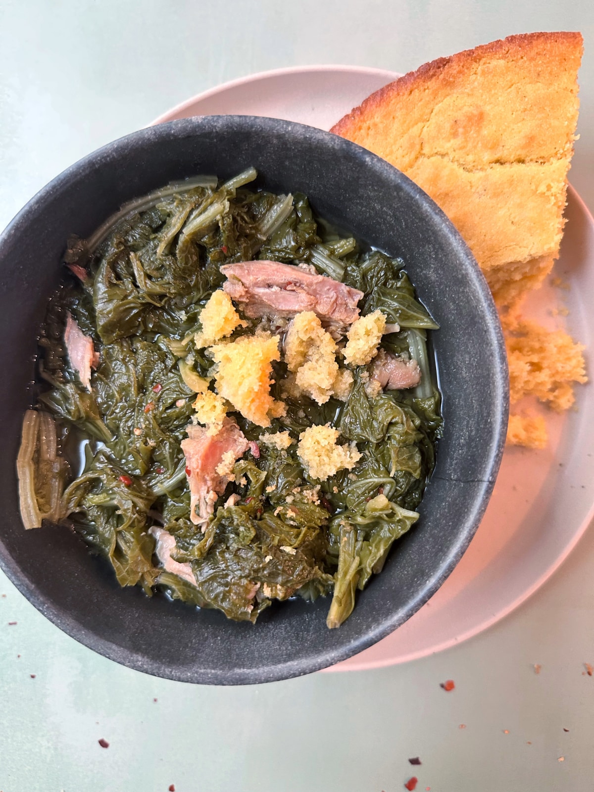A bowl of mustard greens, cooked southern style, with crumbled cornbread on top.