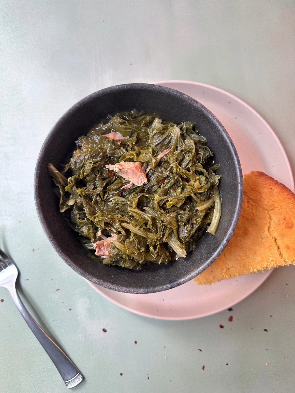 A bowl of mustard greens with cornbread on the side.