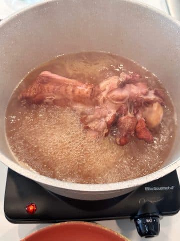 A smoked turkey wing boiling in chicken broth in a large pot.