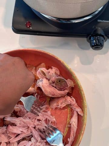 A hand using two forks to shred smoked turkey meat off of its bone.