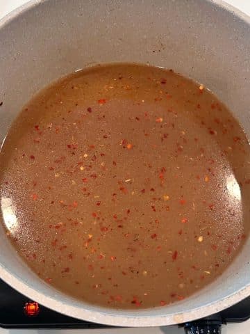 A cream-colored pot filled with seasoned broth.